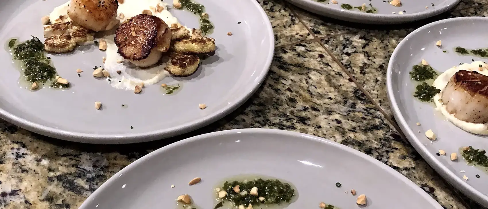 A row of identical scallop courses plated and waiting to be carried to the table