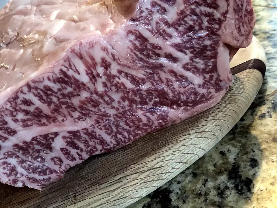 A5 wagyu strip loin showing dense marbling, resting on an oak board