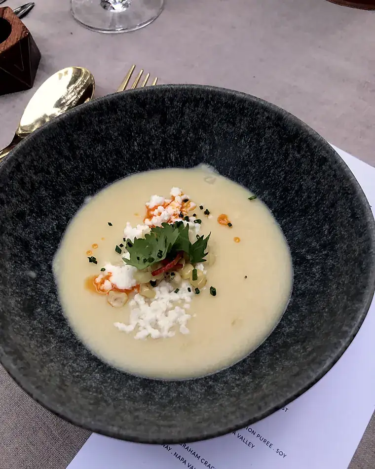 Chilled sweet corn soup with queso fresco, chile and cilantro in a dark bowl