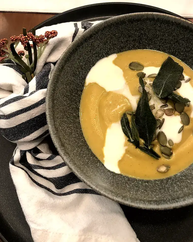 Roasted squash soup with crème fraîche, crisped sage and pepitas in a green ceramic bowl
