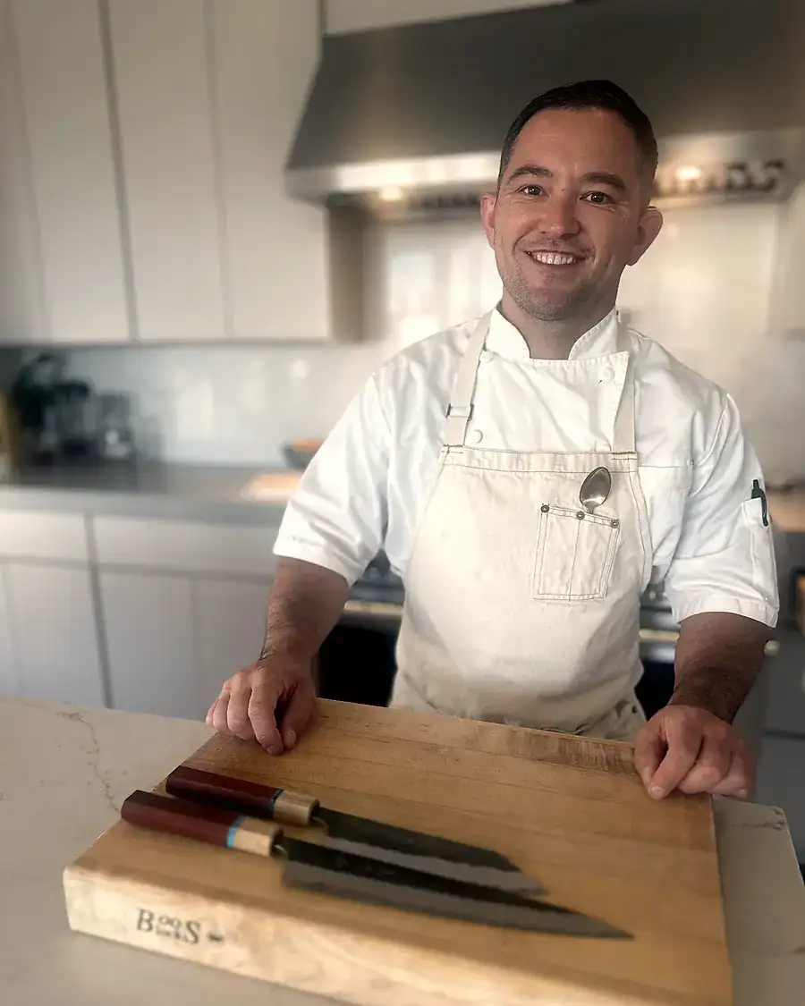 Marc in chef's whites in a kitchen, knives laid out on a cutting board